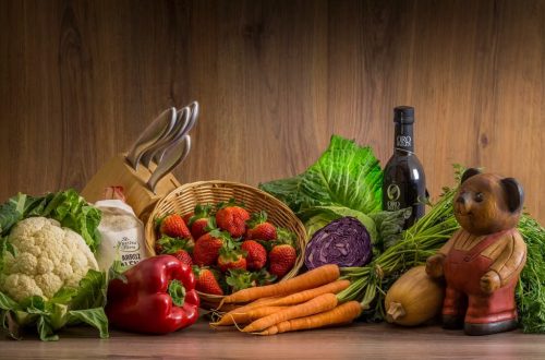 Arrangement of fresh vegetables and fruits on a wooden table with kitchen essentials.