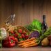 Arrangement of fresh vegetables and fruits on a wooden table with kitchen essentials.
